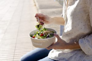 Una mujer come una ensalada Freshkia al aire libre.